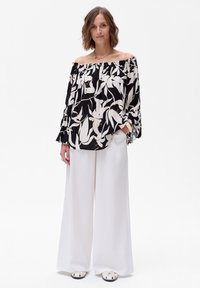Czarna i biała kwiecista bluzka bez ramiączek z bufiastymi rękawami, noszona z szerokimi białymi spodniami. Strój ma luźny krój i miękki materiał.