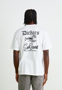 Hvit bomull t-skjorte med et svart grafisk trykk på baksiden, med teksten "Dickies" og "Sea Food Lunch/Dinner," samt en illustrasjon av en hummer.