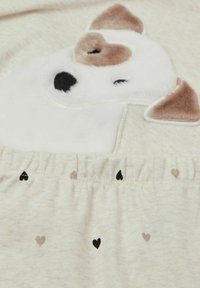 Zachte crèmekleurige stof met een pluizig wit hondenontwerp met bruine accenten. De tailleband heeft kleine zwarte en beige hartjespatronen.