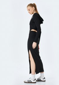Schwarzes geripptes Crop-Top mit Kapuze und einem hochtaillierten Rock mit einem Oberschenkel-Schlitz, kombiniert mit weißen Socken und schwarz gestreiften Sneakers.