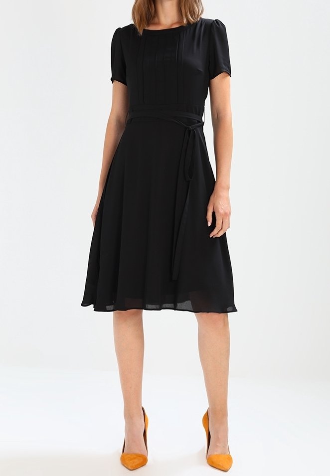 Černé šaty s krátkými puff rukávy, řaseným živůtkem a přiléhavým pasem, který je zdobený uvázaným páskem. Průhledná sukně s volným siluetou.