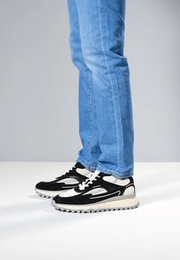 Sneakers in bianco e nero con finitura effetto texture, suola robusta e dettagli in mesh. Indossate con jeans in denim azzurro chiaro.