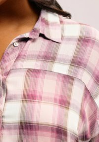 Camicia a scacchi con tonalità di rosa, bianco e marrone, dotata di collo, chiusura a bottoni e taschino sul lato sinistro.
