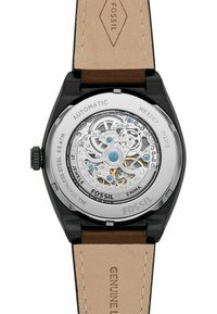 Montre Fossil automatique avec un fond de boîtier transparent révélant un mouvement argenté, des accents bleus, et un boîtier en acier inoxydable noir avec un bracelet en cuir tan.