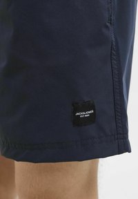 Sötétkék sort sima anyagból, fekete címkével, rajta fehér szöveggel: "JACK & JONES EST. 1990" az alján.
