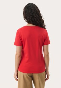 T-shirt en coton rouge avec un col rond et des manches courtes, présentant une texture lisse et une coupe décontractée. Aucuns logos ou motifs visibles.