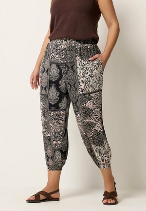 Kvinde iført korte, løstsiddende bukser med paisley-print og elastisk talje, brun ærmeløs top og sandaler.