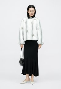 Valge kunstkarusnahast jakk kaunistavate ehtedega, must liibuv kleit voldilise äärega ja teravate varvastega kingad. Lisanditeks must käekott.