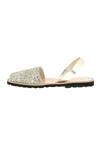 Sandales en paillettes dorées avec une boîte à orteils triangulaire, une sangle métallique au talon et une semelle noire texturée. Doublure intérieure lisse.