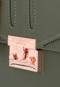 Bolso de mano de cuero texturizado verde con un cierre de metal en color rosa dorado, que cuenta con una placa rectangular y detalles decorativos en los herrajes.
