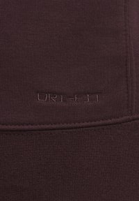 Mørkerød Dri-FIT-stof med ribbet tekstur, der har broderet brandingdetalje. Glat overflade med horisontale og vertikale strikkemønstre.