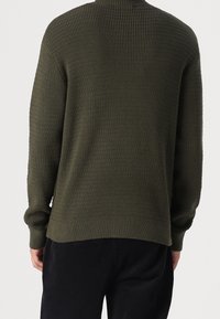 Pull en maille vert foncé avec un motif texturé, poignets et ourlet côtelés, col rond, et coupe décontractée. Semble décontracté et confortable.