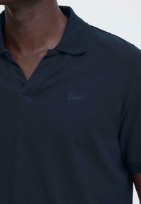 Polo bleu marine en tissu texturé avec un col classique et un discret logo brodé "Blend" sur la poitrine.