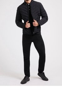 Czarna pikowana kurtka z wysokim kołnierzem i zamkiem, w zestawie z dopasowanymi czarnymi spodniami i czarnymi sneakersami. Gładka tekstura i minimalistyczny design.