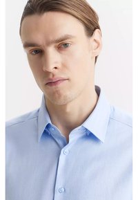 Jasnoniebieska koszula zapinana na guziki o fakturze w jodełkę, z klasycznym kołnierzykiem i dwoma guzikami z przodu.