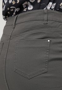 Grå denimjeans med en figurnära design, subtil textur och en liten dekorativ nitt på bakfickan för extra detaljer.