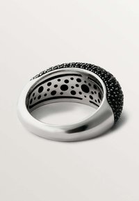 Anillo de plata con una parte superior redondeada cubierta de material negro texturizado y pequeñas esferas, que presenta un interior hueco con recortes circulares.