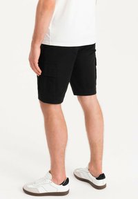 Pantaloni cargo neri in cotone. Presentano due tasche laterali e una linea dritta. Abbinati a sneaker bianche con un'accents nera sul tallone.