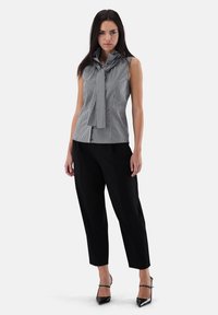 Gray and white checkered sleeveless top with a tied neck detail, paired with black tapered trousers and black high-heeled shoes.