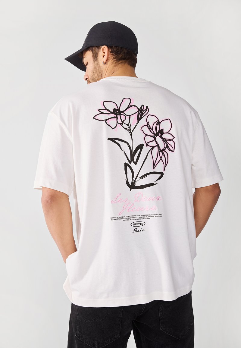 White cotton t-shirt with a loose fit, featuring black and pink floral illustrations on the back and text detailing.