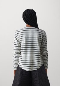 Langarmshirt in hellgrau mit schwarzen horizontalen Streifen, weicher Textur, abgerundetem Saum, kombiniert mit einem schwarzen steppierten Rock.
