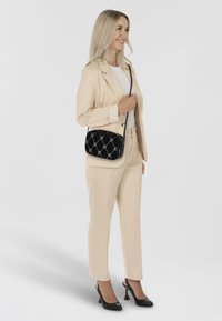 Traje beige a medida con una chaqueta ajustada y pantalones entallados, acompañado de un bolso de hombro negro con estampado y tacones negros. Textura suave.