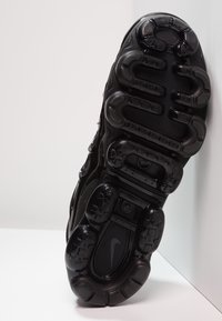 Zwarte sportieve schoen met een gestructureerde rubberen zool, opvallende dempingse segmenten, een hoekig ontwerp en het prominente Nike-logo op de hiel.