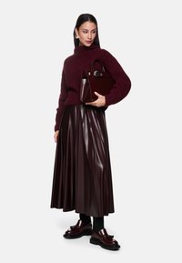 Bordeaux gebreide trui, geplooide faux leren rok en glanzende bordeaux loafers. Gestructureerde handtas met een ronde sluiting.