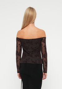Off-shoulder topp i mørk brun stoff med gjennomsiktige lange ermer, blomsterdesign og en tettsittende fasong. Glatt tekstur med et rent preg.