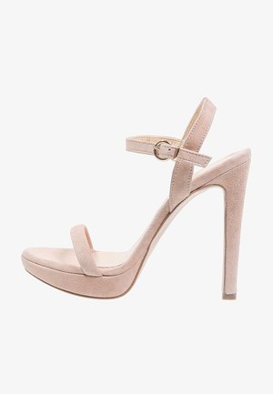 Sandalia de tacón alto de ante beige con plataforma, tira en el tobillo y hebilla en tono dorado. Presenta una puntera cerrada y un acabado texturizado.