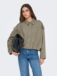 Olivengrønn oversized jakke med en strukturert krage, med en jevn tekstur og trekvart-ermer, kombinert med blå denimjeans og en svart veske.