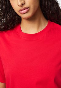 Rød, kortærmet bomulds t-shirt med en klassisk rund halsudskæring og glat tekstur, der har diskrete syningsdetaljer langs kraven.