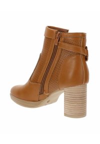 Stivaletto marrone in pelle con lati perforati, zip laterale e tacco rotondo impilato. Presenta una superficie liscia e un design elegante.