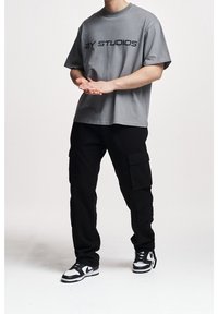 Harmaa lyhythihainen t-paita, jossa on musta "2Y STUDIOS" -logo, yhdistetty mustiin taskuhousuihin, joissa on sivutaskut, ja valko-mustiin tennareihin.