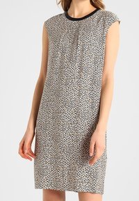 Mönstrad ärmlös klänning med rund halsringning och lös passform. Texturerad vit bas med svarta och gyllene abstrakta mönster.