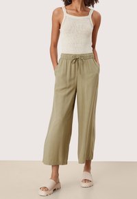 Lekki oliwkowozielone spodnie o szerokich nogawkach z elastycznym ściągaczem i wiązaniem w talii, zestawione z kremowym dzianinowym topem na ramiączkach i beżowymi butami wsuwanymi.