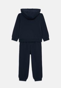 Chándal de dos piezas en azul marino hecho de un tejido suave; incluye una sudadera con capucha y pantalones a juego con cintura y puños elásticos.