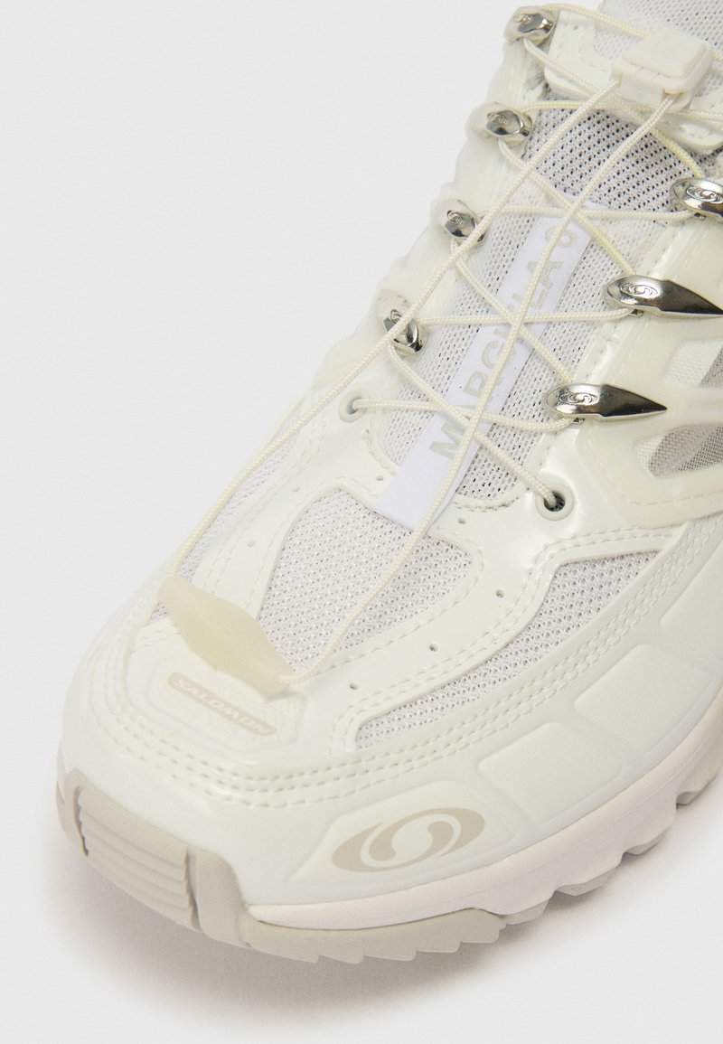 Vita sneakers med meshtopp, gummisula och silverdetaljer. Har elastiska snören och en strukturerad yta för bättre grepp.