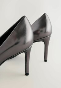 Hochhackige Schuhe aus metallisch grauem Leder mit spitzem Zehenbereich, schlankem Design und glänzender Oberfläche mit schwarzen Akzenten an den Absätzen.