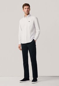 Camisa blanca de botones con un bolsillo en el pecho, combinada con pantalones negros y zapatillas negras. Diseño sencillo, textura suave y líneas limpias.