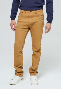 Jean en denim beige avec une coupe droite, dotée de poches avant et d'une fermeture à bouton en métal. Associé à des baskets blanches et un pull bleu marine.