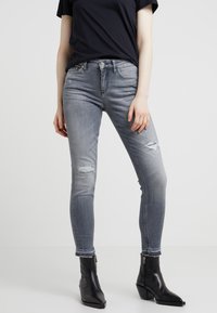 Smal jeans i blekt grå denim med slitna områden vid knäna. Kombineras med svarta ankelboots som har en elegant design och smal ben.