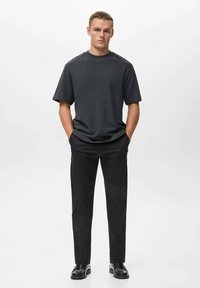 Krátký rukáv tmavě šedého trička, volný střih, v kombinaci s černými kalhotami a černými botami, jednoduchý design, hladká textura, bez vzorů.