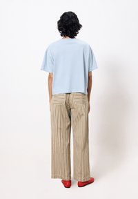 Helles blaues Baumwoll-T-Shirt mit kurzen Ärmeln; kombiniert mit braunen und weißen gestreiften weiten Hosen und roten Ballerinas.