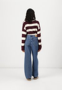Weinroter und cremefarbener gestreifter Pullover; weit geschnittene blaue Jeans mit Gesäßtaschen; kombiniert mit beigen Schuhen; strukturierte Stoffe, lässige Passform.