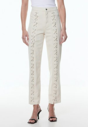 Die cremefarbenen Hose mit Schnürdetails an den Seiten, weichem Stoff, geradem Schnitt und klassischem Knopfverschluss.