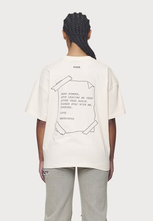 Person mit geflochtenem Haar trägt ein weißes, übergroßes T-Shirt mit einer Grafik eines aufgeklebt wirkenden Zettels und Text auf der Rückseite, der den Wunsch ausdrückt, dass der Sommer bleiben soll.