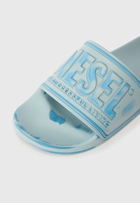 Sandale en caoutchouc légère de couleur bleue avec un dessus texturé, logo "DIESEL" en relief et une semelle lisse. Présente des accents d'un bleu plus foncé subtil.