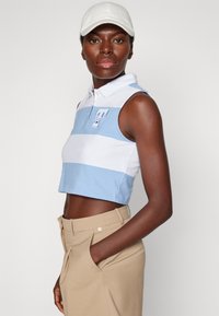Top tipo polo recortado en azul claro y rayas blancas, con cuello y logo bordado. Combinado con pantalones beige entallados, que cuentan con bolsillos.