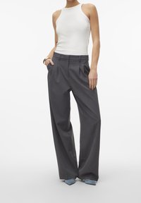 Široké šedé kalhoty s předními plicemi, v kombinaci s přiléhavým bílým topem bez rukávů. Doplnené světle modrými lodičkami se špičatou špičkou.